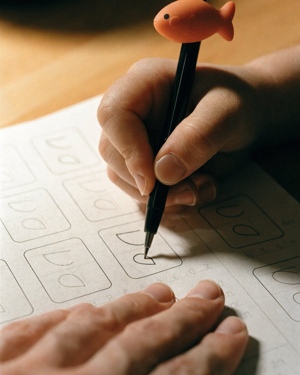Gros plan sur une main qui trace une lettre dans le cahier Ecrilo, le stylo tenu grâce au guide-doigts orange